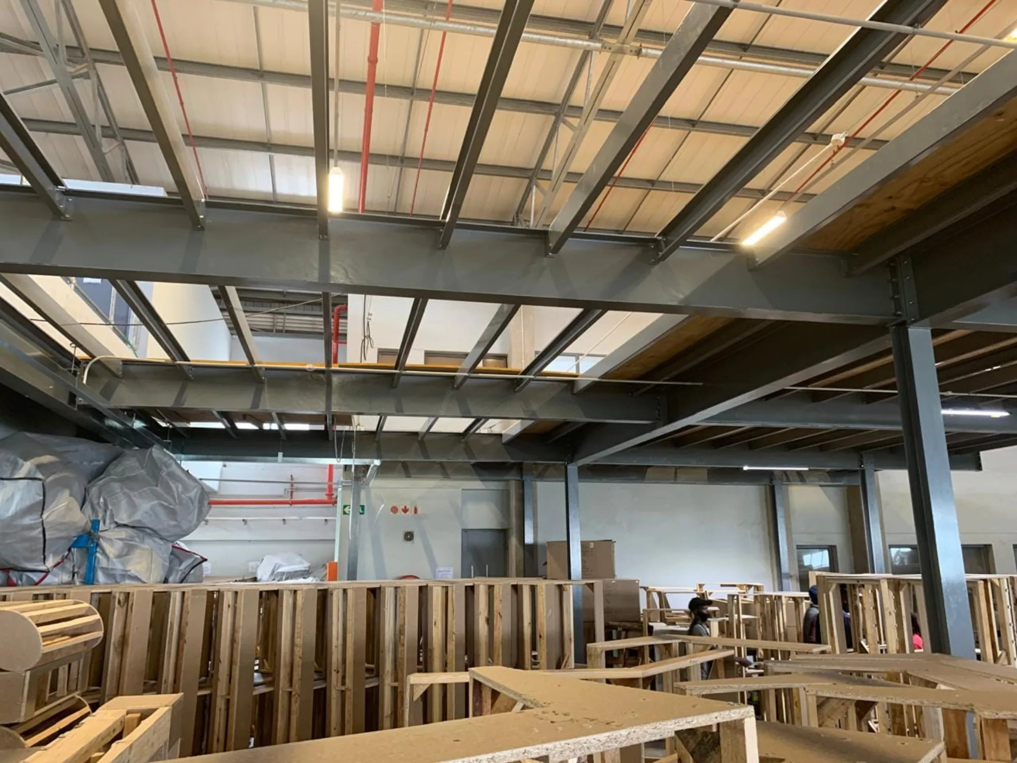 Painted steel beams and joists forming the mezzanine frame above the factory floor